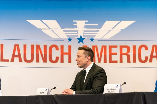 Elon Musk sitting in front of a graphic that says Launch America