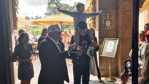 Donald Trump showing something to Elon Musk who holds his son on his shoulders